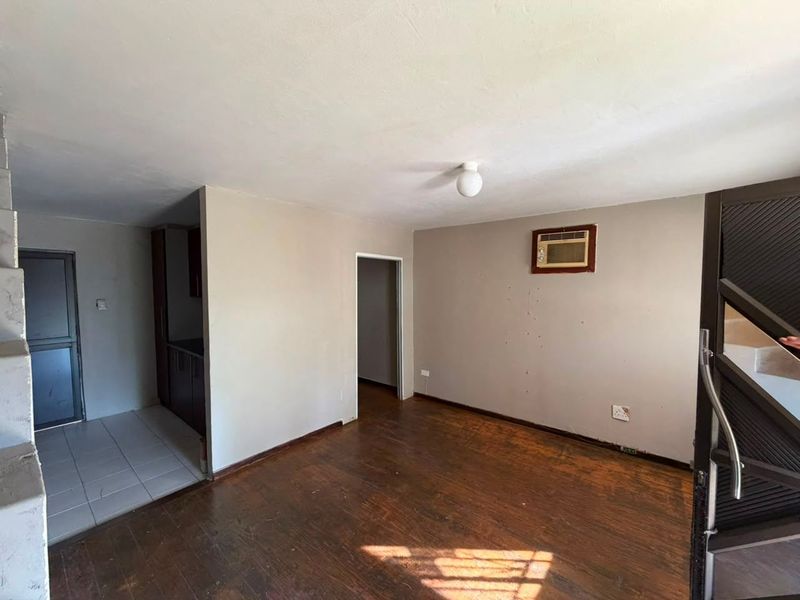 An empty open-plan living area featuring worn hardwood flooring, neutral wall tones, and a built-in wall air conditioning unit.