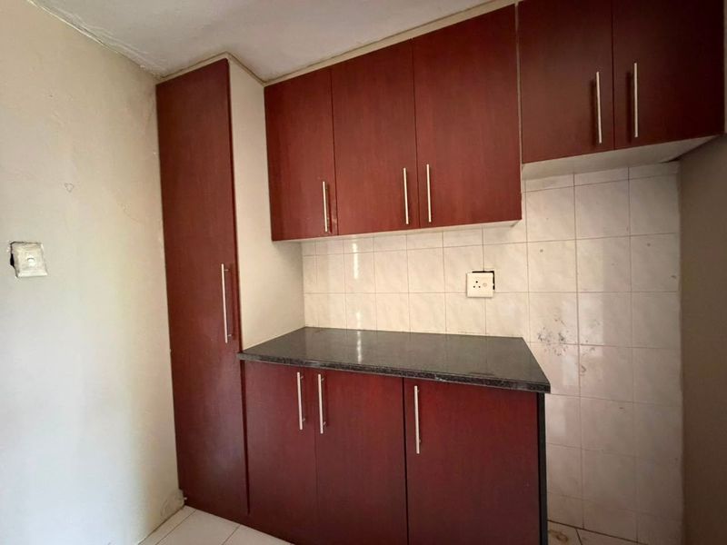 A compact kitchen area featuring dark wood-look cabinetry, stone countertops, and a tiled backsplash, currently vacant and ready for updates.