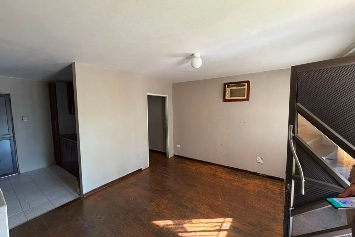 An empty living room featuring hardwood flooring, a wall-mounted air conditioning unit, and a secure entrance gate, offering a blank canvas for renovation.