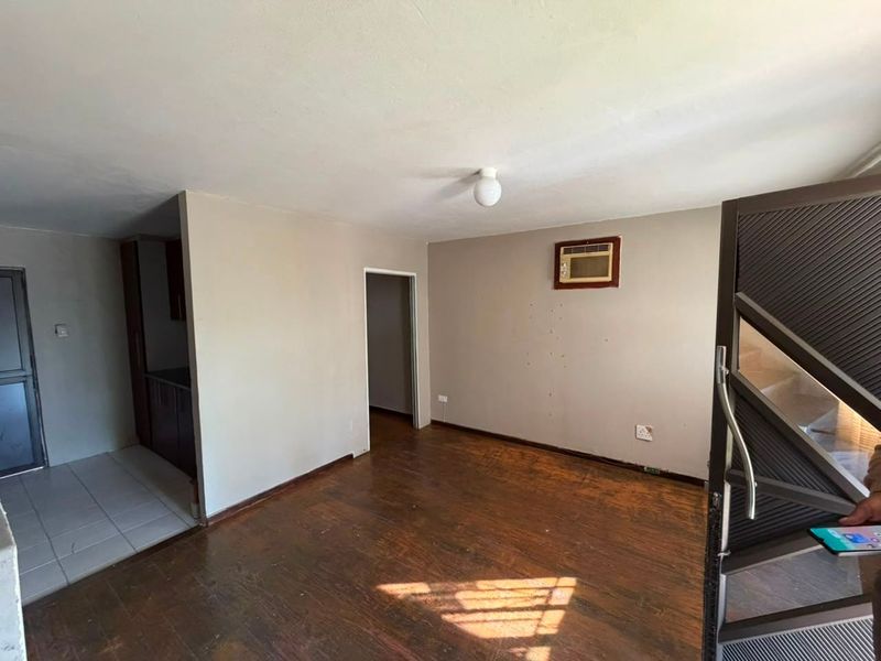 An empty living room featuring hardwood flooring, a wall-mounted air conditioning unit, and a secure entrance gate, offering a blank canvas for renovation.