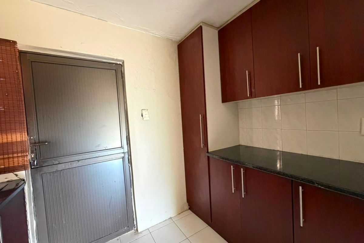 A compact kitchen area featuring dark wood-look cabinetry, dark countertops, and tiled flooring, providing a functional space ready for modernization.