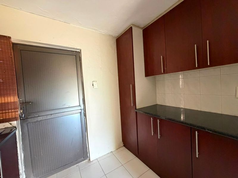 A compact kitchen area featuring dark wood-look cabinetry, dark countertops, and tiled flooring, providing a functional space ready for modernization.