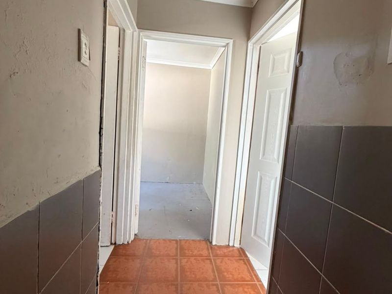A narrow hallway featuring tiled flooring and partial wall tiling, currently in need of cosmetic repairs and finishing to improve its overall condition.