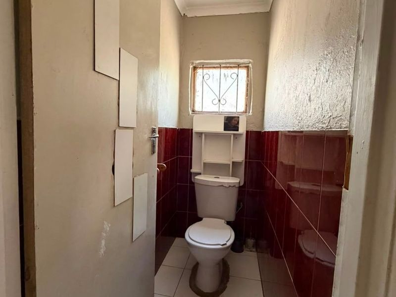 A compact guest bathroom featuring tiled walls, a standard toilet, and a small window with security bars.