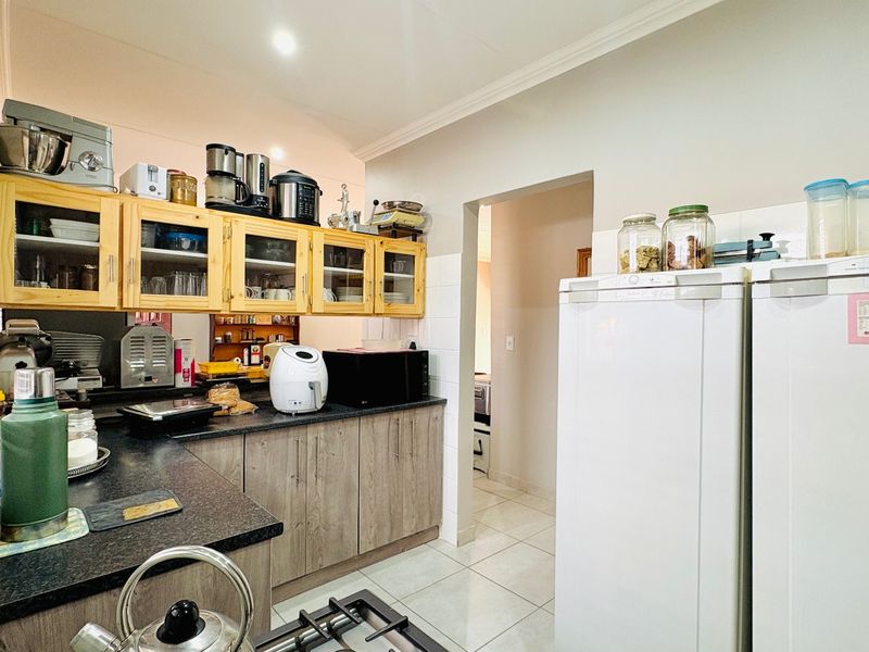 A functional kitchen featuring laminate cabinetry, dark countertops, tiled flooring, and a gas hob, with a doorway leading to an adjacent space.