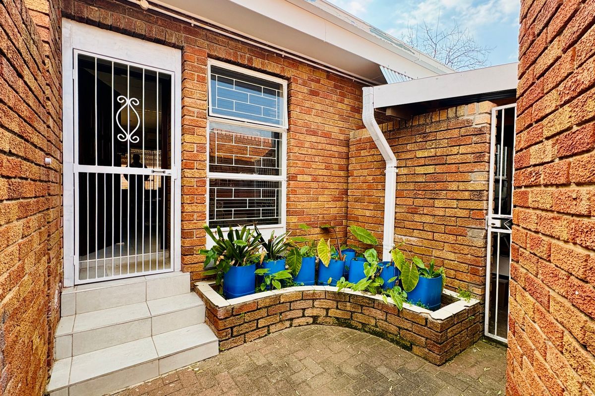 A private rear courtyard featuring exposed brick walls, a paved patio area, a built-in brick planter, and secure access points.