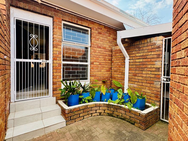 A private rear courtyard featuring exposed brick walls, a paved patio area, a built-in brick planter, and secure access points.