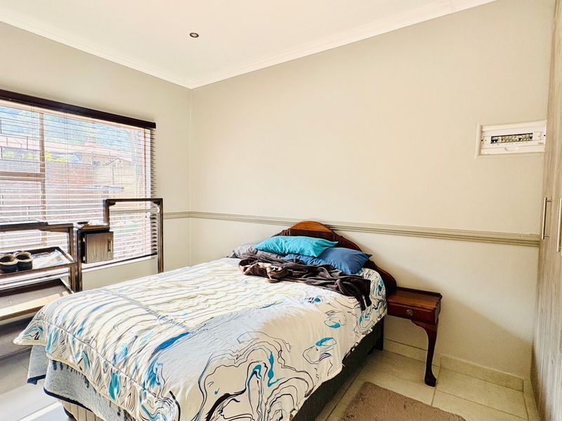 A well-lit bedroom featuring built-in cupboards, tiled flooring, and a large window with venetian blinds, providing a functional and comfortable living space.