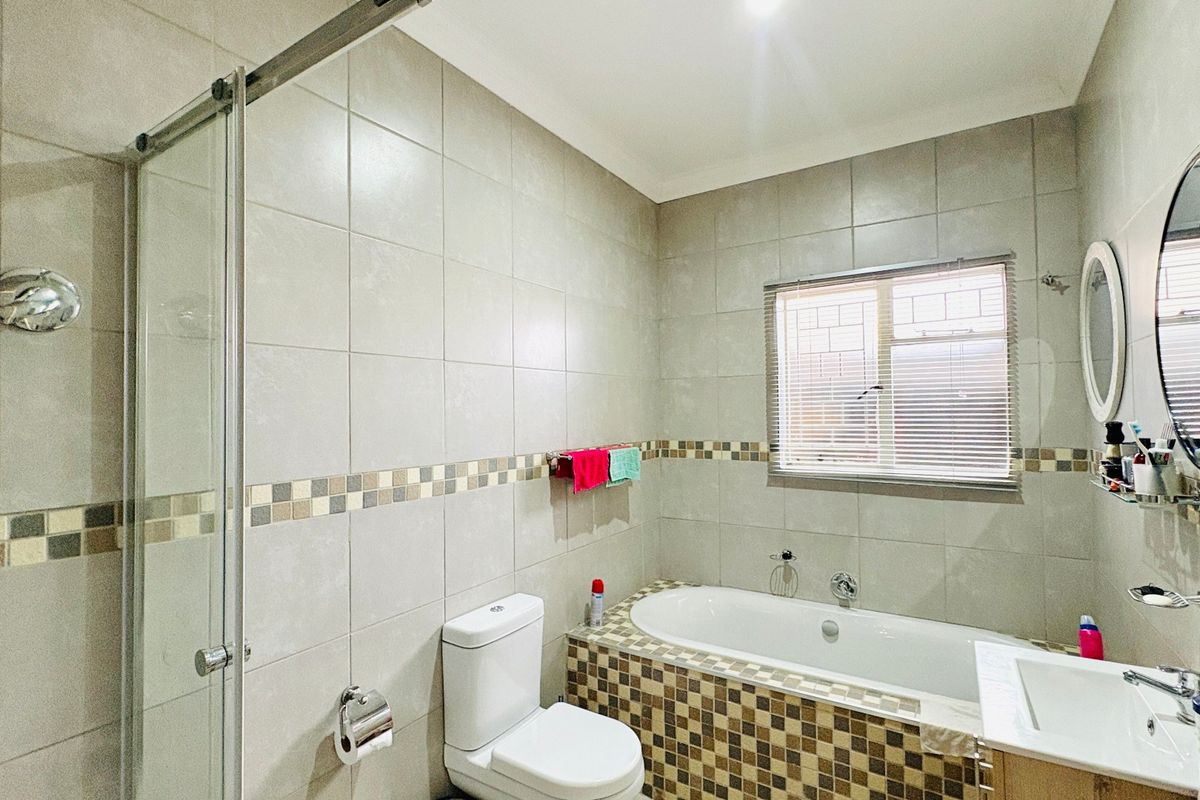 A well-maintained bathroom featuring a glass-enclosed shower, a built-in bathtub with mosaic tile detailing, a vanity basin, and neutral wall tiling.