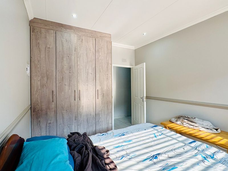 A well-maintained bedroom featuring neutral walls, coving, recessed downlighting, and ample built-in cupboard storage.