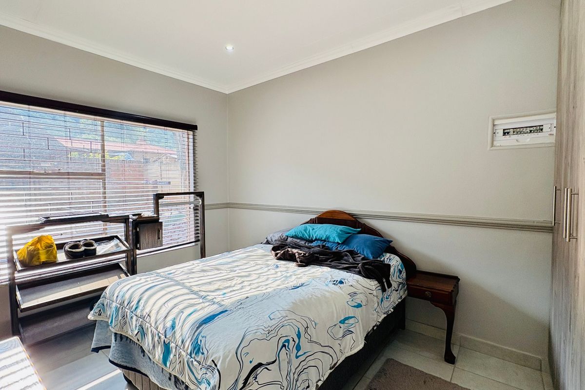 A bedroom featuring built-in cupboards, tiled flooring, and a window with venetian blinds.