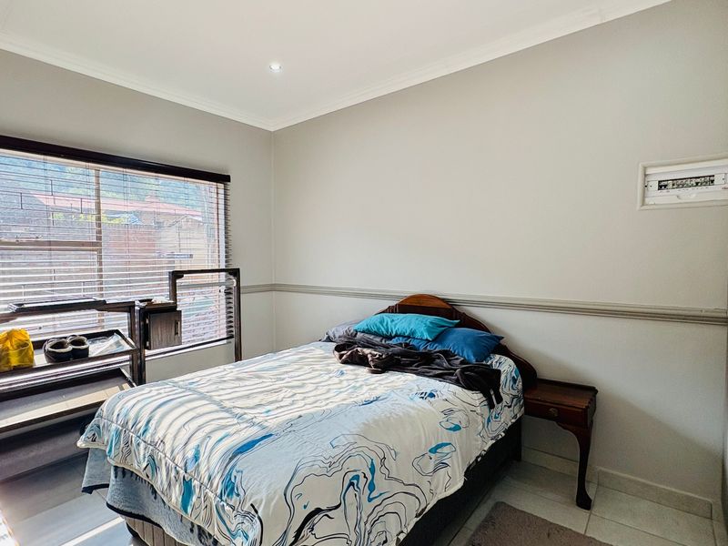 A bedroom featuring built-in cupboards, tiled flooring, and a window with venetian blinds.