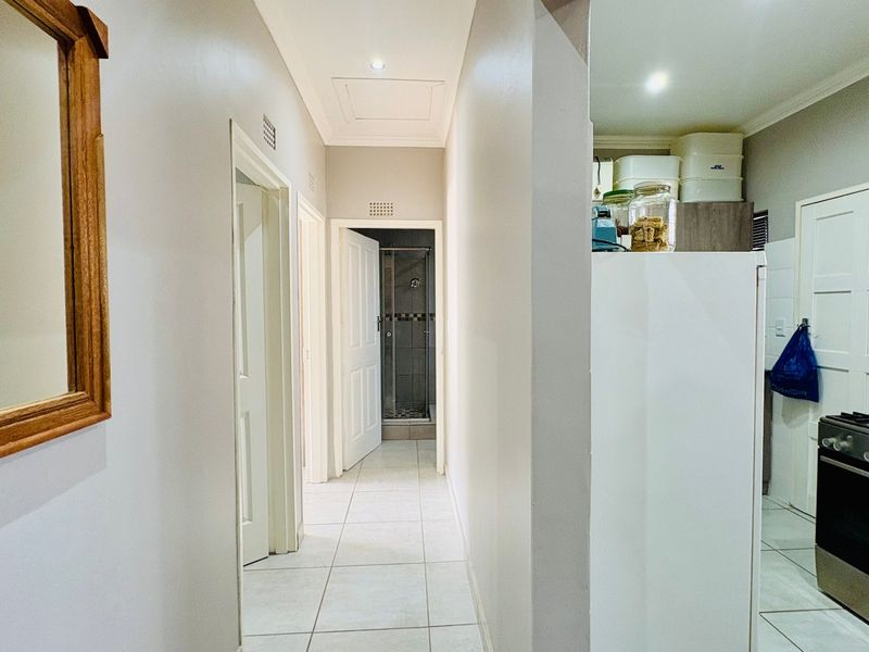 A bright hallway with tiled flooring leading to a bathroom and kitchen area, featuring neutral walls and recessed lighting.
