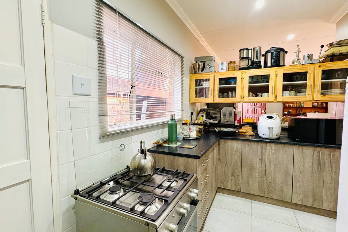 Functional kitchen featuring gas stove, laminate cabinetry, dark countertops, and tiled backsplash with natural light from a window with venetian blinds.