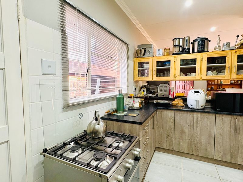 Functional kitchen featuring gas stove, laminate cabinetry, dark countertops, and tiled backsplash with natural light from a window with venetian blinds.