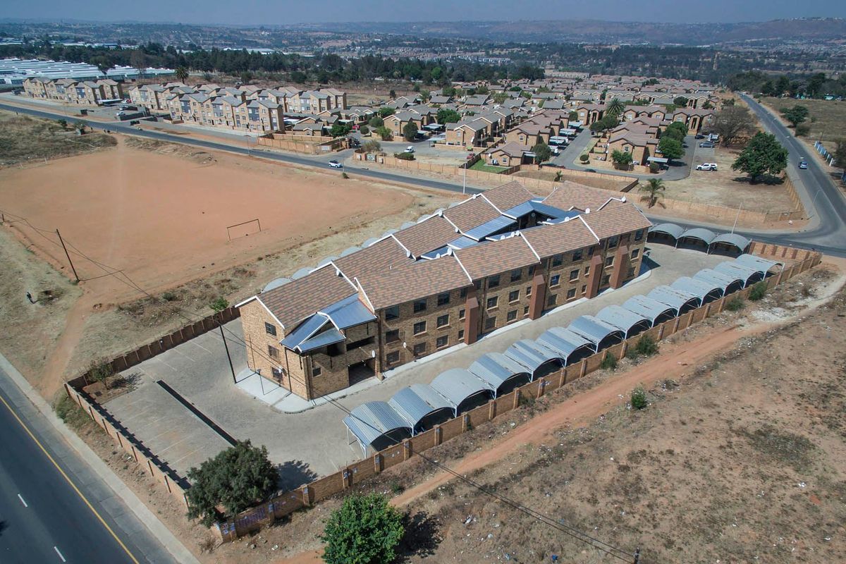 Aerial view of a multi-story apartment complex featuring a tiled roof, brick exterior, and dedicated carport parking bays within a secure perimeter.