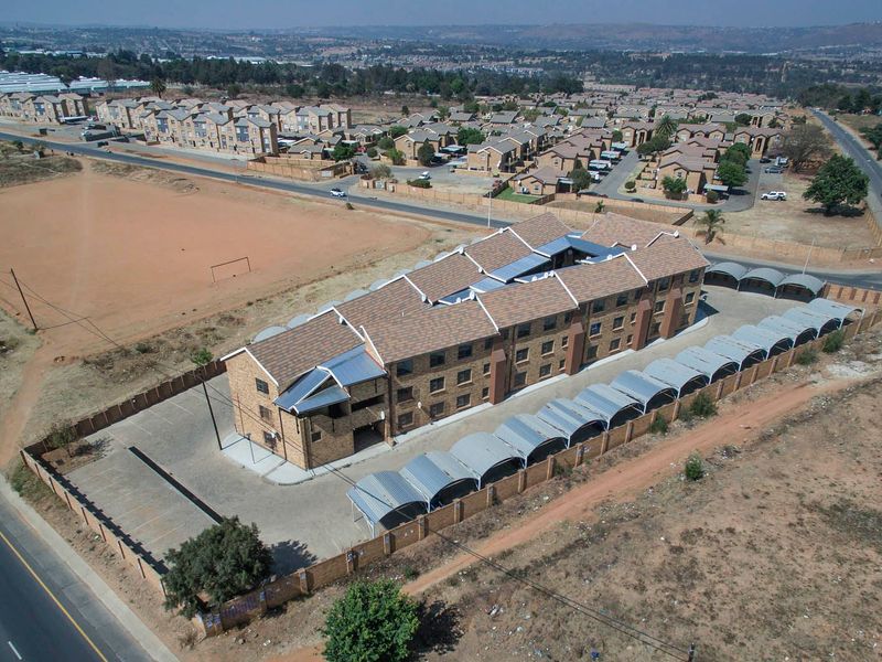 Aerial view of a multi-story apartment complex featuring a tiled roof, brick exterior, and dedicated carport parking bays within a secure perimeter.