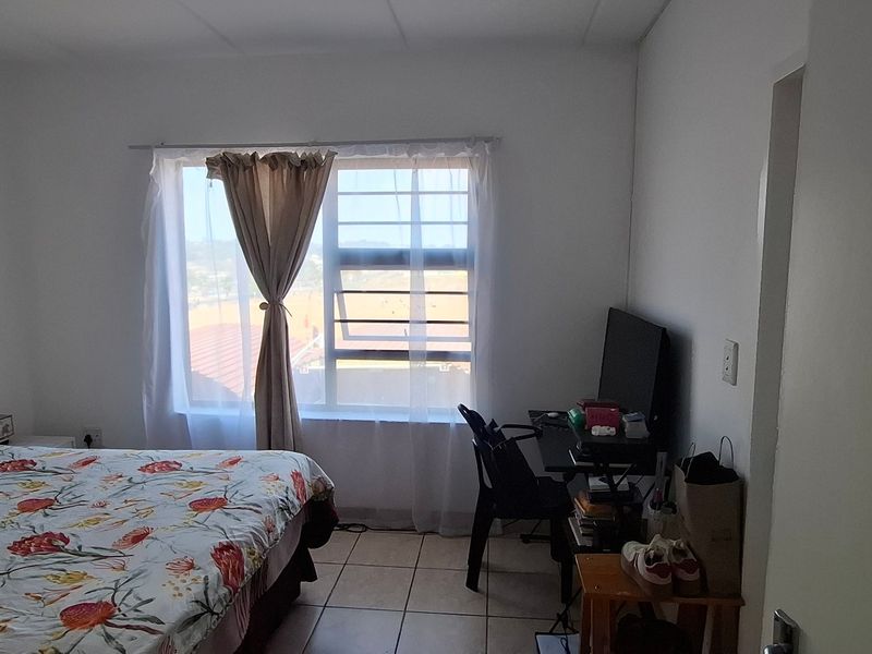 A functional bedroom featuring tiled flooring and a window fitted with security bars, offering a simple and practical living space.