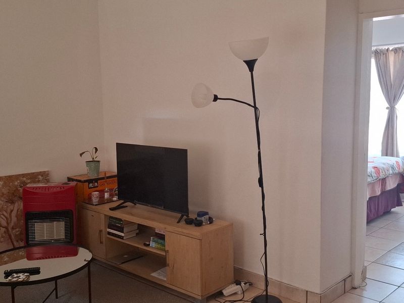 A living room area with neutral walls and tiled flooring, providing access to an adjacent bedroom space.