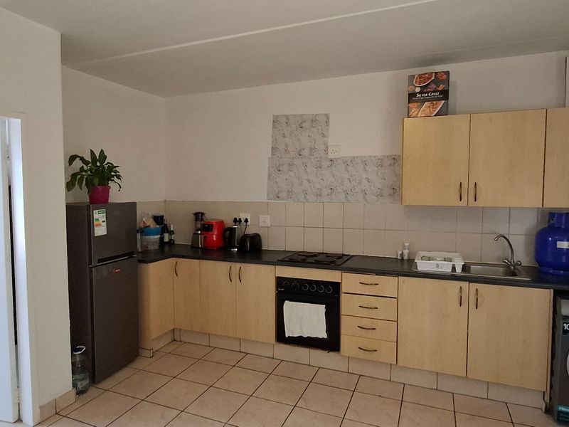 Functional kitchen featuring light wood cabinetry, laminate countertops, built-in oven with gas hob, and tiled flooring with a tiled backsplash area.