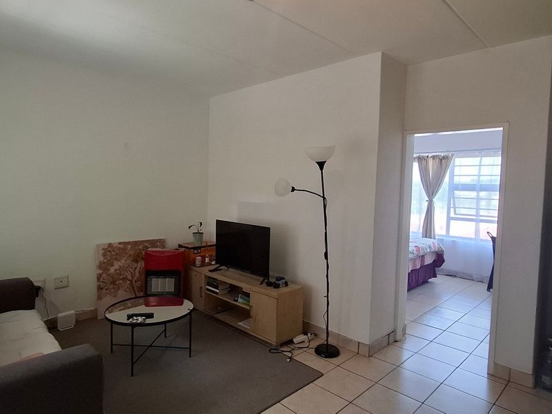 A living area featuring tiled flooring and an exposed electrical distribution board, with an open transition leading into an adjacent bedroom space.