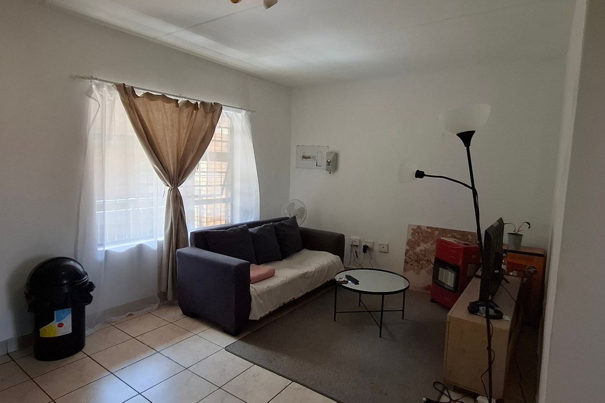 A compact living room featuring tiled flooring, a window with security bars, and an exposed electrical distribution board on the wall.