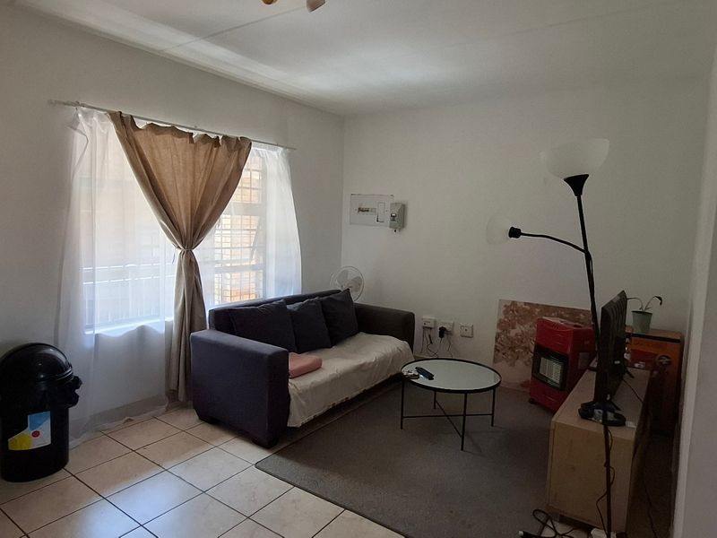 A compact living room featuring tiled flooring, a window with security bars, and an exposed electrical distribution board on the wall.