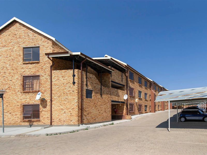 Exterior view of a multi-story apartment complex featuring face brick construction, paved driveway, and covered parking bays.