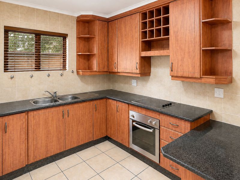 A functional kitchen featuring wood-look cabinetry, granite countertops, a built-in oven, electric hob, and a double stainless steel sink with tiled finishes.