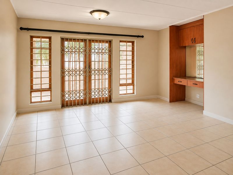 Spacious living area featuring neutral tiled flooring, built-in wooden desk with cabinetry, and sliding glass doors with security gates leading to the exterior.