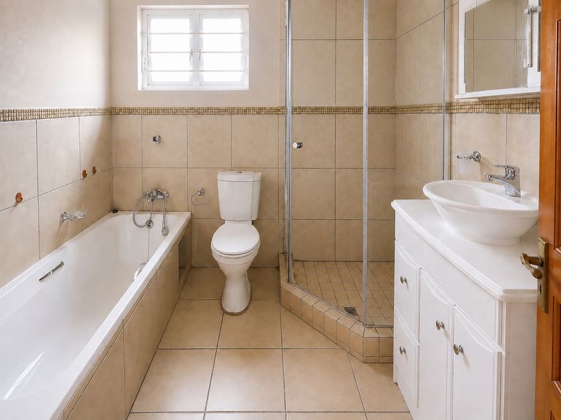 A functional bathroom featuring a bathtub, separate shower enclosure, vessel sink with vanity cabinet, and neutral floor-to-ceiling tiling.