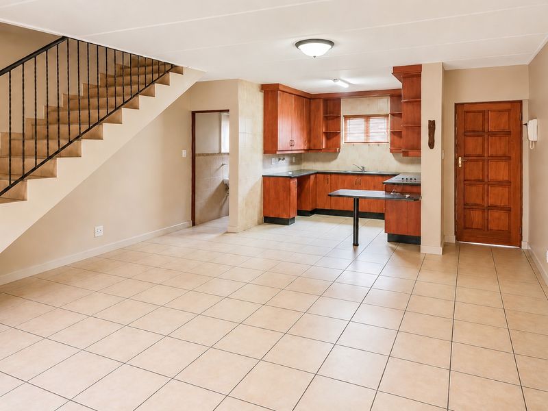 Open-plan living area featuring tiled flooring, a staircase with wrought iron balustrade, and a functional kitchen with built-in cabinetry and breakfast bar.