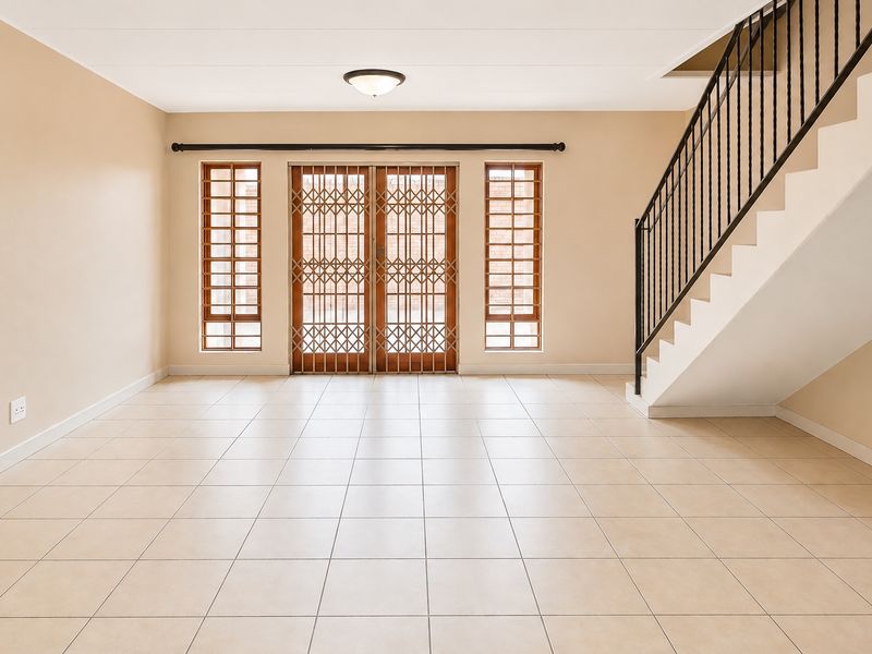 Spacious, empty living area featuring neutral ceramic floor tiles, a staircase with a metal balustrade, and secure access to the exterior.