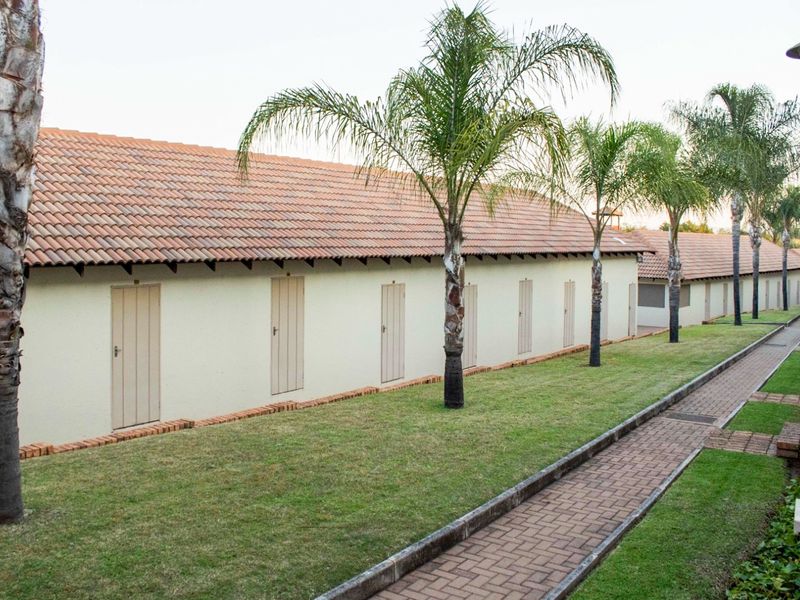 A view of the townhouse exterior featuring a long row of units with individual access doors, terracotta roofing, and a paved garden walkway.