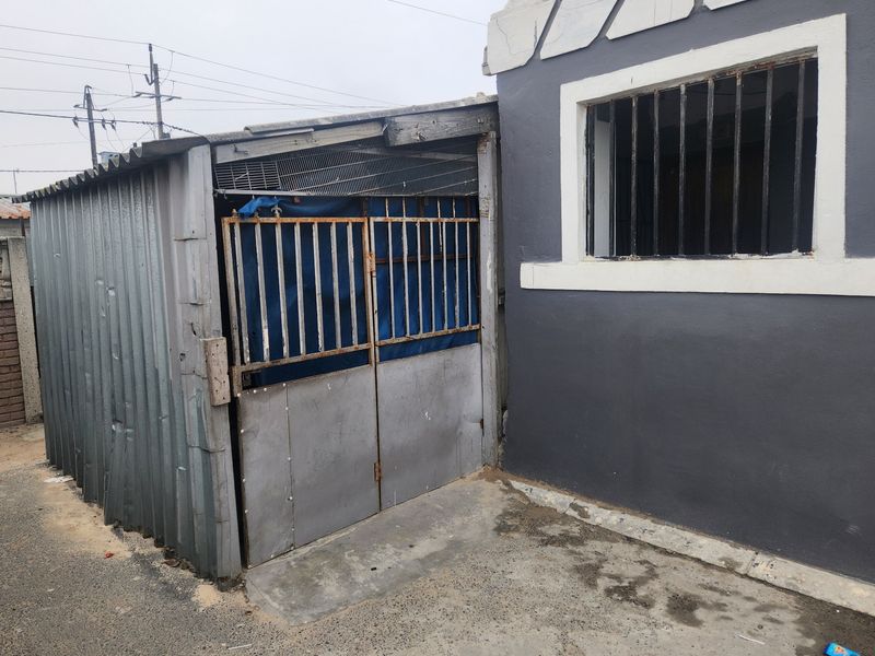 Exterior view of a property featuring a corrugated metal structure with a security gate and a window with security bars.
