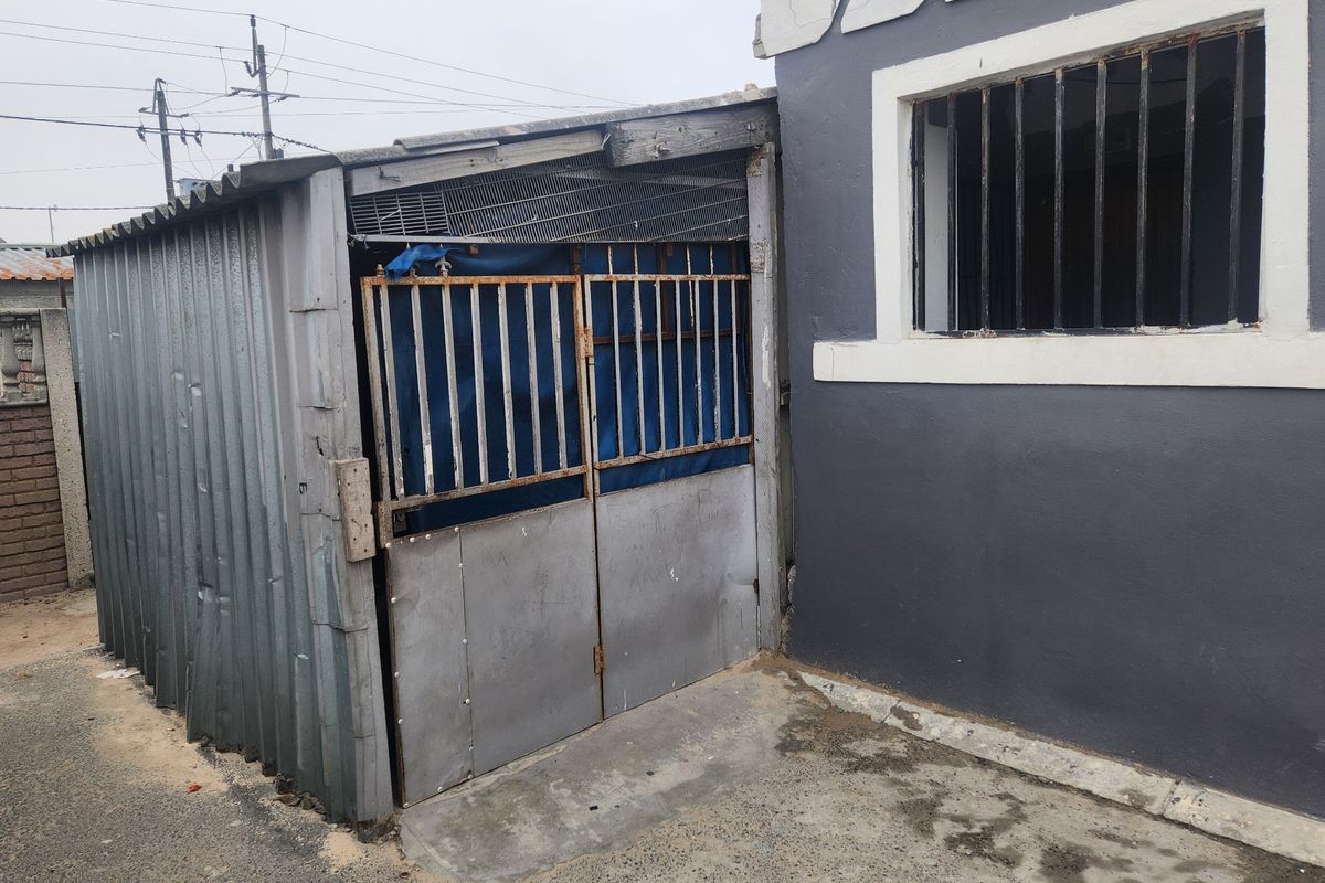 A rear exterior view showing a corrugated metal structure attached to the main building, featuring security bars and concrete paving.
