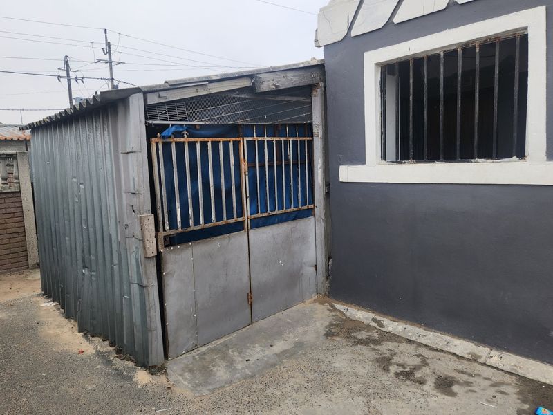 A rear exterior view showing a corrugated metal structure attached to the main building, featuring security bars and concrete paving.