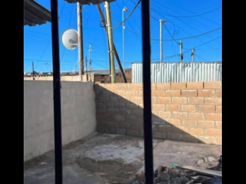 An outdoor rear area featuring a concrete block boundary wall and concrete slab flooring, currently in an unfinished state.