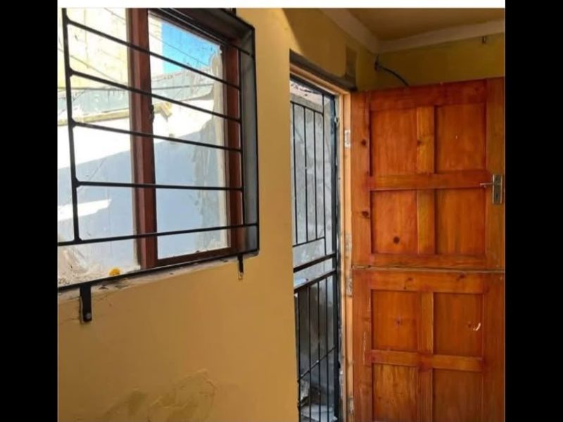 A small interior hallway featuring a timber door and window with security bars, showing signs of wear on the wall surfaces.