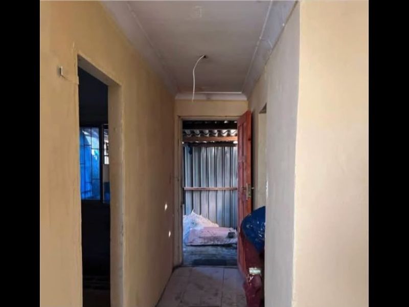 A narrow hallway showing signs of wear with exposed electrical wiring and unfinished wall surfaces, requiring cosmetic updates and repairs.