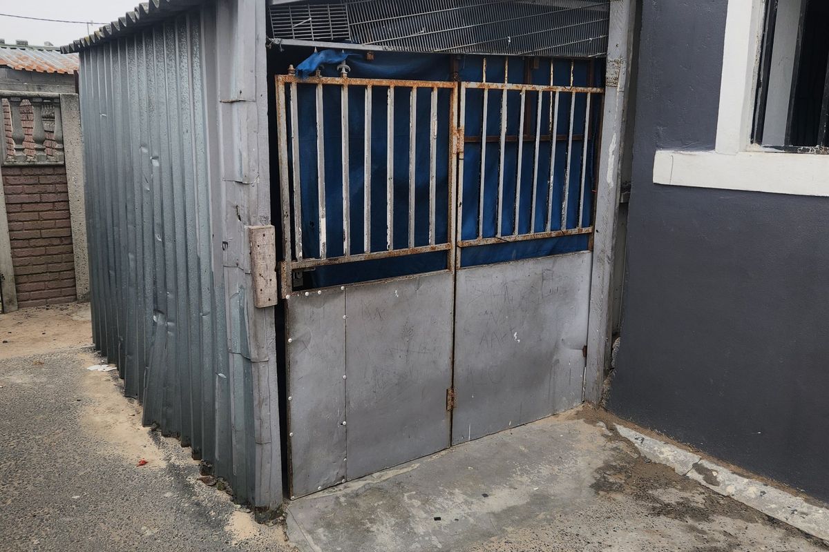 A utilitarian corrugated metal structure attached to the side of the house, featuring a metal gate and concrete flooring.