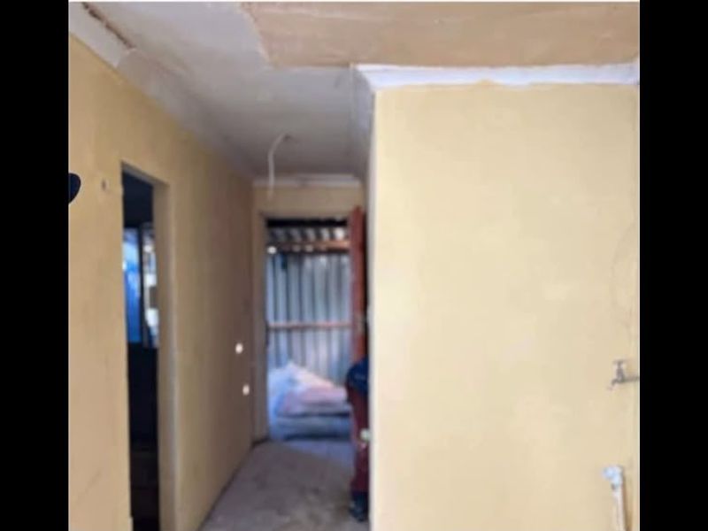A narrow hallway area in a state of renovation, featuring unfinished wall surfaces and exposed electrical wiring.