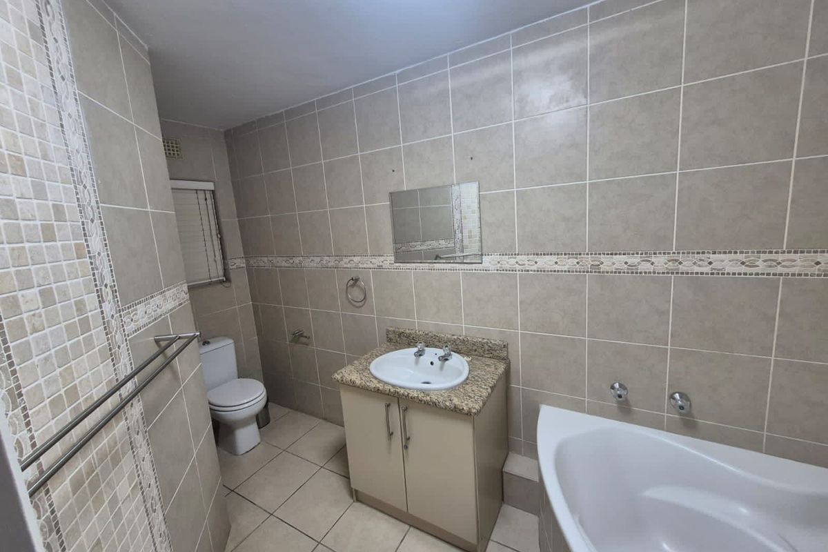 A functional bathroom featuring neutral wall and floor tiling, a vanity with granite countertop, a bathtub, and a standard toilet.