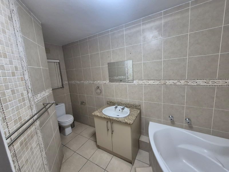 A functional bathroom featuring neutral wall and floor tiling, a vanity with granite countertop, a bathtub, and a standard toilet.