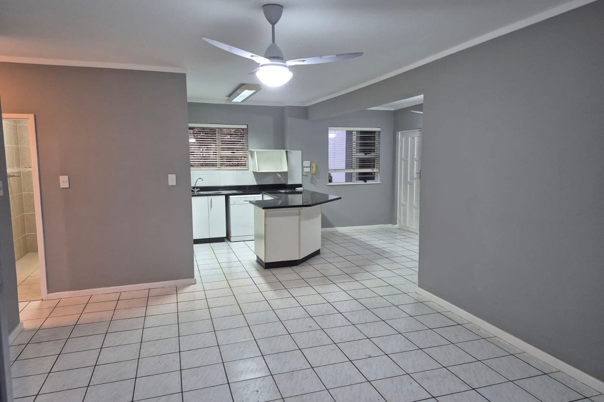 Spacious open-plan living and kitchen area featuring tiled flooring, a central kitchen island with stone countertops, and neutral grey wall finishes.