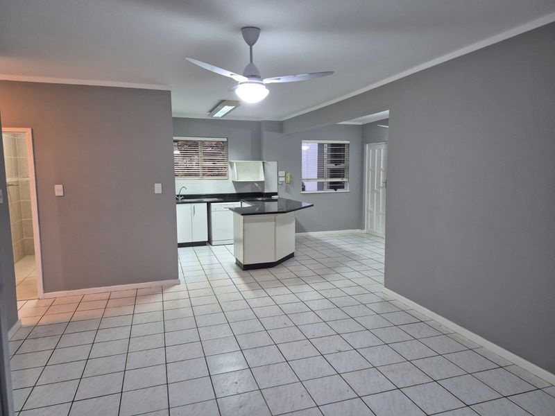 Spacious open-plan living and kitchen area featuring tiled flooring, a central kitchen island with stone countertops, and neutral grey wall finishes.