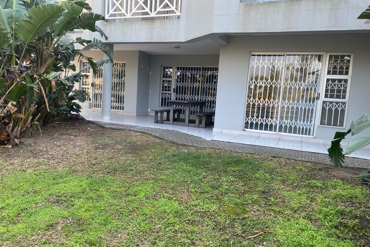 Rear view of the apartment building featuring a tiled patio area, security gates on sliding doors, and a balcony above.