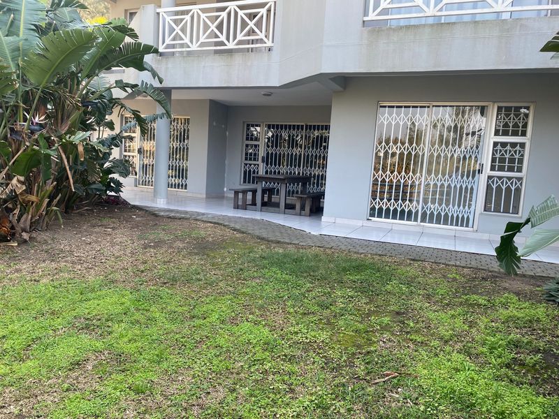 Rear view of the apartment building featuring a tiled patio area, security gates on sliding doors, and a balcony above.