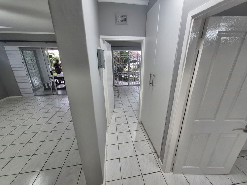 A functional hallway featuring tiled flooring, built-in storage cupboards, and a security gate leading to an outdoor area.