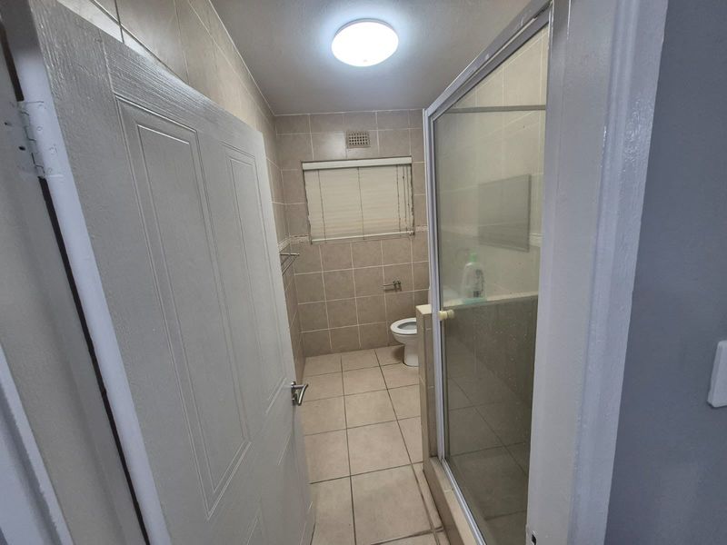 A functional bathroom featuring a shower enclosure, toilet, and neutral floor-to-ceiling wall tiling, offering a clean and practical layout.